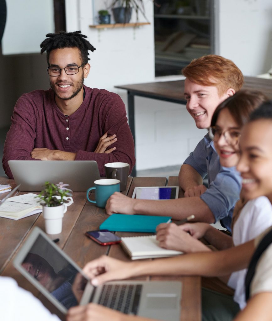 Gruppe an Personen, die lachen und Laptops vor sich stehen haben