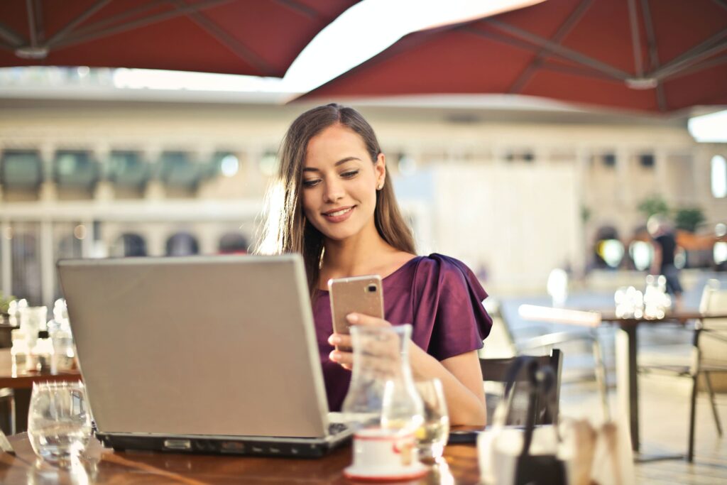 Frau an einem Bistrotisch im Café mit Laptop und Smartphone