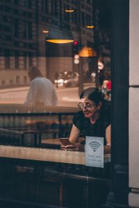 Frau in einem Café, auf dessen Glasscheibe "Free WiFi" steht