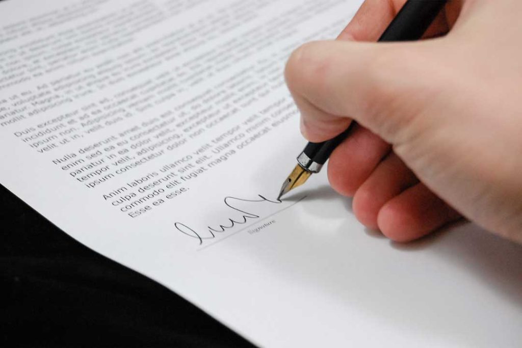 Das Bild zeigt eine Nahaufnahme, wie ein Vertrag unterschrieben wird.