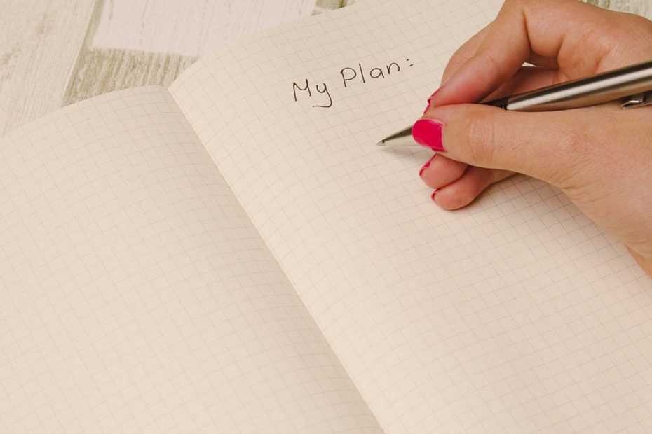 Das Bild zeigt eine Hand, welche mit einem Kugelschreiber einen Plan schreibt.